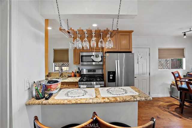 kitchen with stainless steel appliances, brown cabinetry, wood finished floors, a peninsula, and baseboards