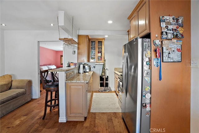 kitchen featuring recessed lighting, a peninsula, a breakfast bar, wood finished floors, and glass insert cabinets