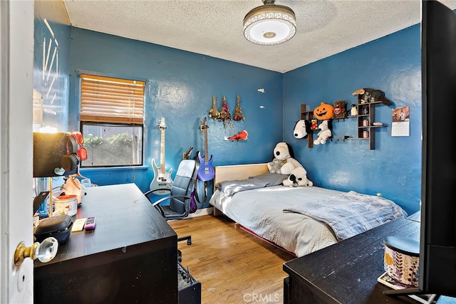 bedroom featuring a textured ceiling, baseboards, wood finished floors, and a textured wall