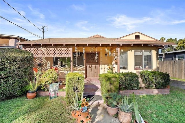 view of front of house with covered porch, fence, a front lawn, and stucco siding