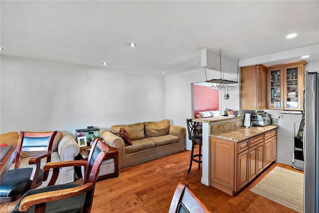 kitchen with open floor plan, light wood finished floors, a kitchen breakfast bar, and a peninsula