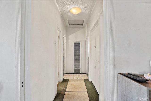 corridor featuring attic access, a heating unit, a textured ceiling, and carpet flooring