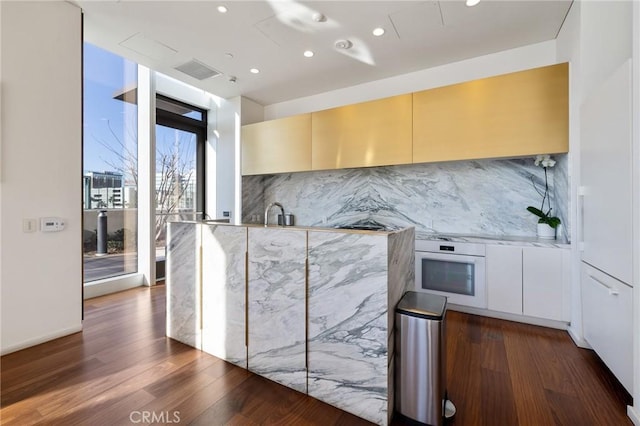 kitchen featuring visible vents, dark wood-style floors, modern cabinets, white oven, and backsplash