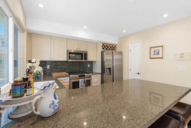 kitchen featuring a breakfast bar area, stainless steel appliances, a peninsula, decorative backsplash, and dark stone counters