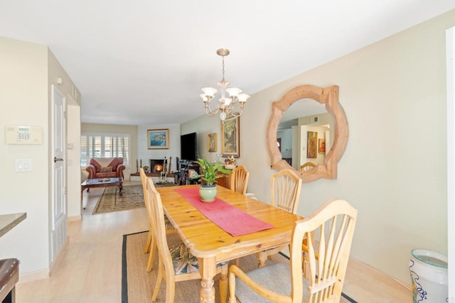 dining room with a large fireplace, light wood-style flooring, baseboards, and a notable chandelier