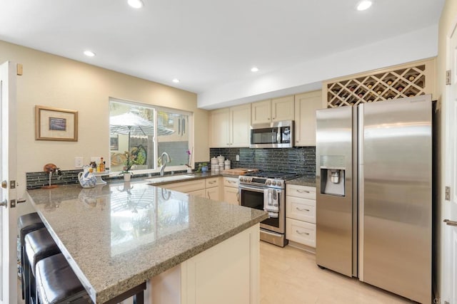 kitchen featuring light stone counters, recessed lighting, backsplash, appliances with stainless steel finishes, and a peninsula