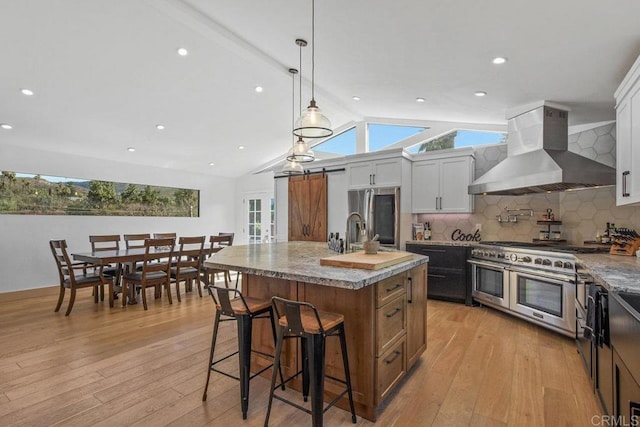 kitchen with appliances with stainless steel finishes, a breakfast bar, light wood-style flooring, and wall chimney range hood