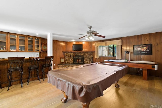 playroom featuring bar, ceiling fan, pool table, a stone fireplace, and light wood-type flooring