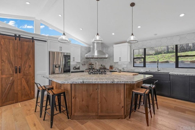 kitchen featuring a sink, white cabinetry, light wood-style floors, wall chimney range hood, and light stone countertops