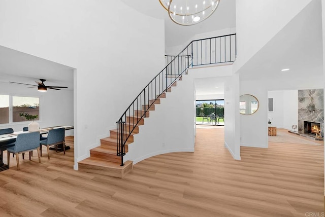 stairs featuring a towering ceiling, a premium fireplace, wood finished floors, baseboards, and ceiling fan with notable chandelier