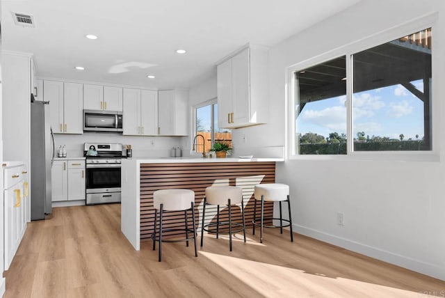 kitchen featuring visible vents, white cabinets, light wood-style flooring, a peninsula, and stainless steel appliances