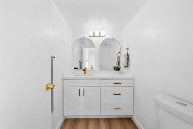 bathroom featuring toilet, baseboards, wood finished floors, and vanity