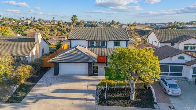 traditional home featuring an attached garage, fence, a tiled roof, driveway, and a residential view