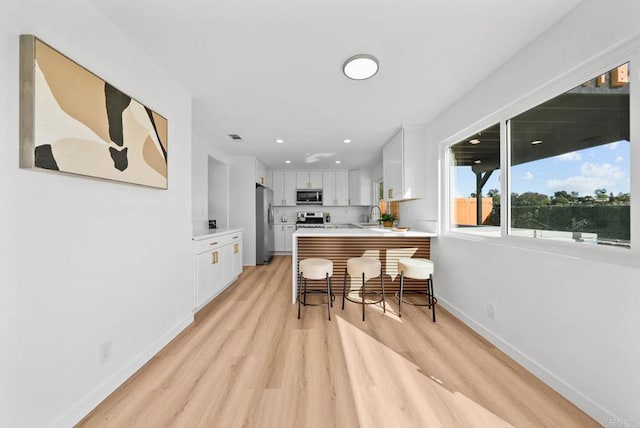 kitchen with stainless steel appliances, a peninsula, white cabinets, light countertops, and light wood-type flooring