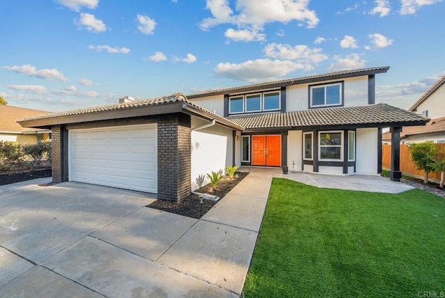 view of front of home featuring a garage, concrete driveway, a tiled roof, a front yard, and stucco siding