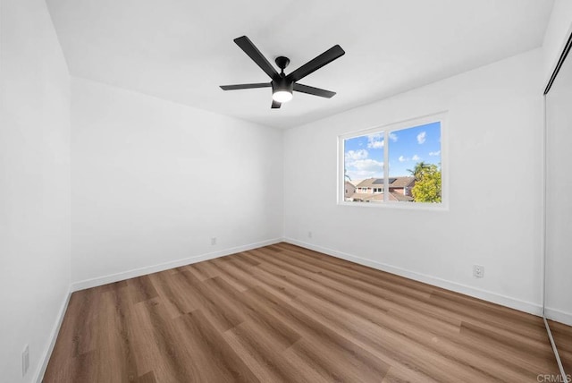 spare room with wood finished floors, a ceiling fan, and baseboards