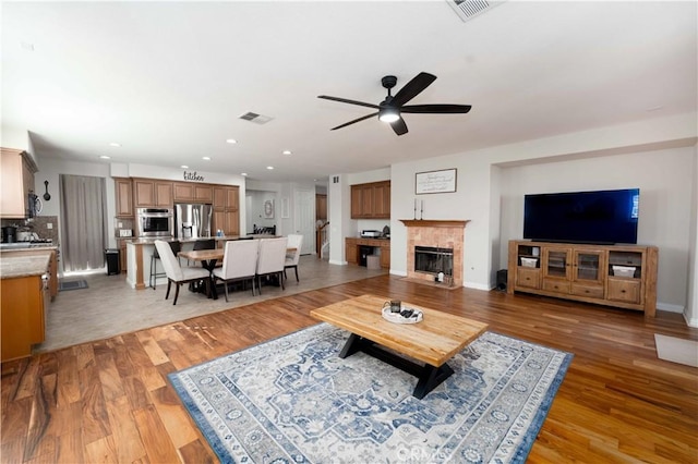 living room with light wood finished floors, a tile fireplace, visible vents, and a ceiling fan