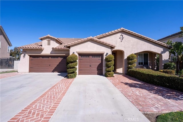 mediterranean / spanish house featuring a garage, a tiled roof, concrete driveway, and stucco siding