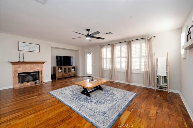 living area with a tile fireplace, wood finished floors, a ceiling fan, visible vents, and baseboards