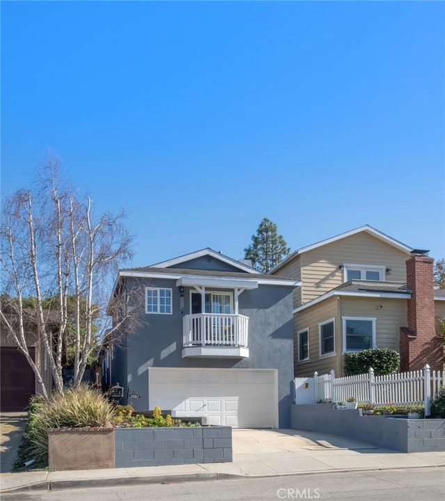 view of front of home featuring a garage, concrete driveway, a balcony, fence, and stucco siding