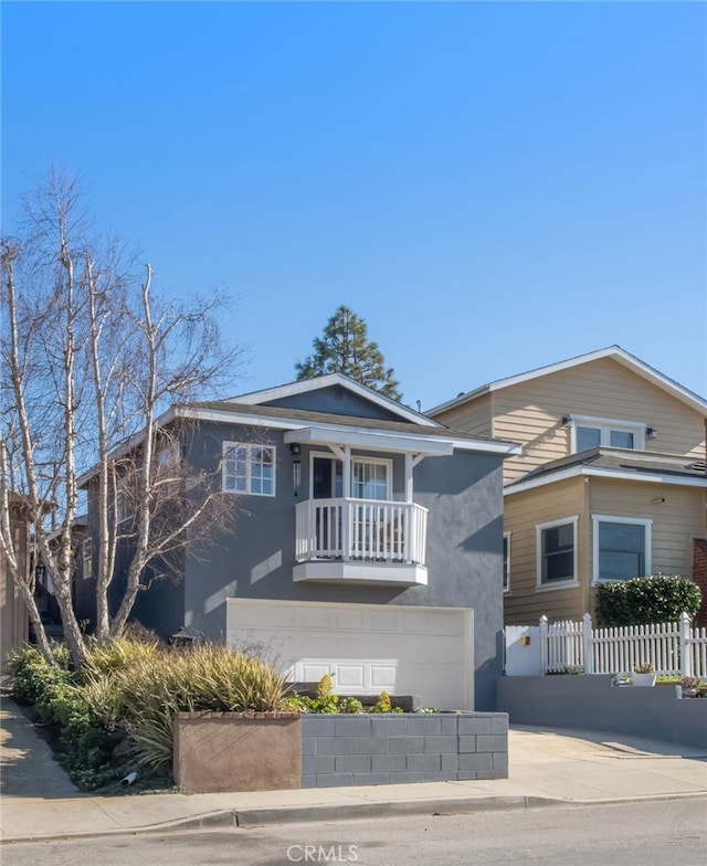 view of front of home with stucco siding, concrete driveway, fence, a balcony, and a garage