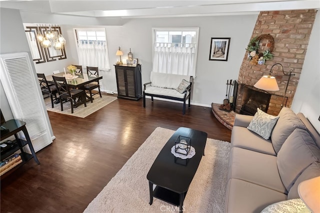 living room featuring a brick fireplace, wood finished floors, an inviting chandelier, and baseboards