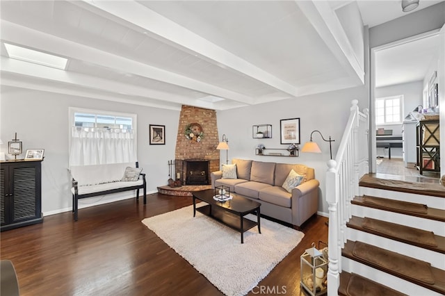 living area with a skylight, a brick fireplace, wood finished floors, and beamed ceiling