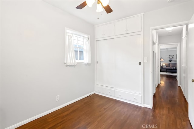 unfurnished bedroom featuring dark wood-style floors, a closet, a ceiling fan, and baseboards