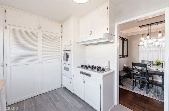 kitchen featuring stainless steel gas stovetop, light countertops, light wood-style flooring, and under cabinet range hood