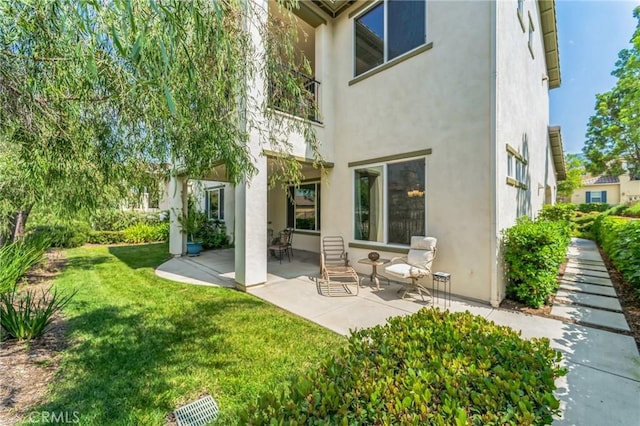 rear view of house featuring a patio area, a lawn, and stucco siding