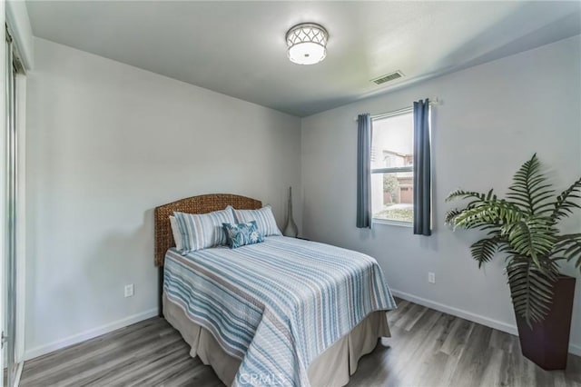 bedroom with baseboards, visible vents, and wood finished floors