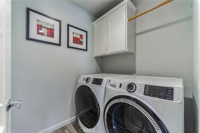 clothes washing area featuring washing machine and dryer, cabinet space, baseboards, and wood finished floors