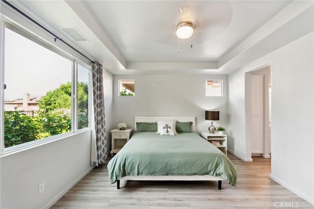 bedroom with a raised ceiling, light wood finished floors, and baseboards