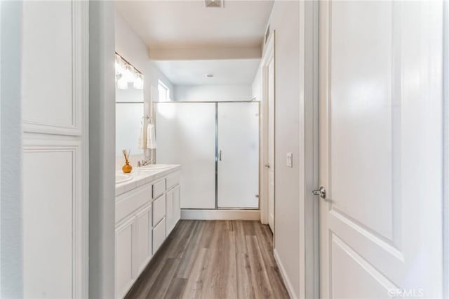 bathroom featuring double vanity, a shower stall, a sink, and wood finished floors