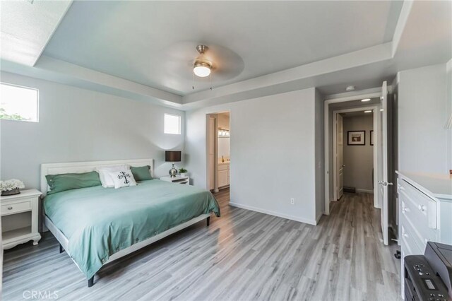 bedroom with a tray ceiling, baseboards, multiple windows, and light wood finished floors