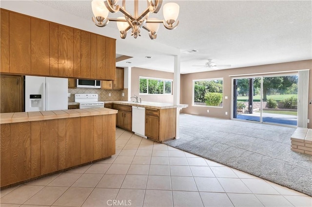 kitchen featuring open floor plan, a peninsula, white appliances, and brown cabinets