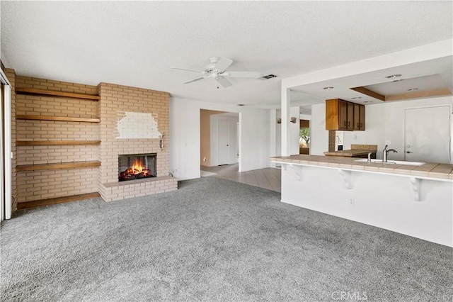 unfurnished living room with a fireplace, visible vents, carpet flooring, a sink, and ceiling fan