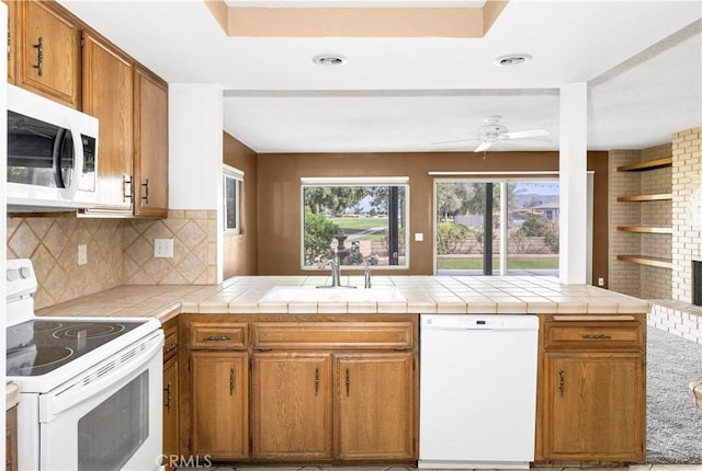 kitchen featuring a peninsula, white appliances, a sink, brown cabinets, and decorative backsplash