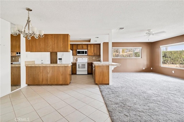 kitchen with white appliances, brown cabinets, open floor plan, a peninsula, and light countertops