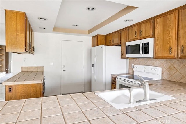 kitchen with tile countertops, white appliances, a tray ceiling, and a sink