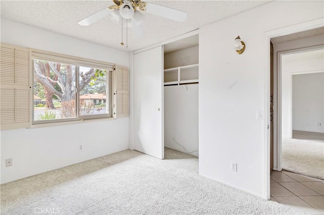 unfurnished bedroom featuring light carpet, a textured ceiling, light tile patterned flooring, and a closet