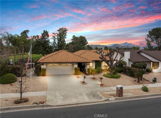 view of front of house with a garage, concrete driveway, a tiled roof, a mountain view, and stucco siding