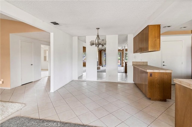 kitchen featuring a textured ceiling, brown cabinetry, light tile patterned flooring, and a notable chandelier