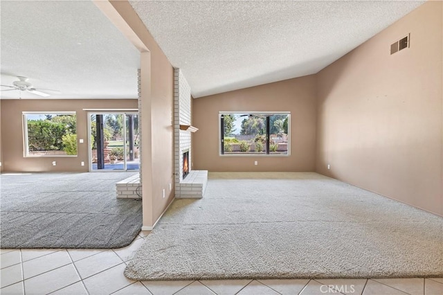 carpeted empty room featuring visible vents, a ceiling fan, lofted ceiling, a textured ceiling, and a brick fireplace