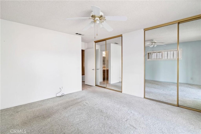 unfurnished bedroom featuring visible vents, ceiling fan, a textured ceiling, carpet flooring, and multiple closets