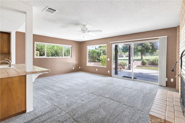 unfurnished living room featuring a textured ceiling, light colored carpet, a sink, visible vents, and a ceiling fan