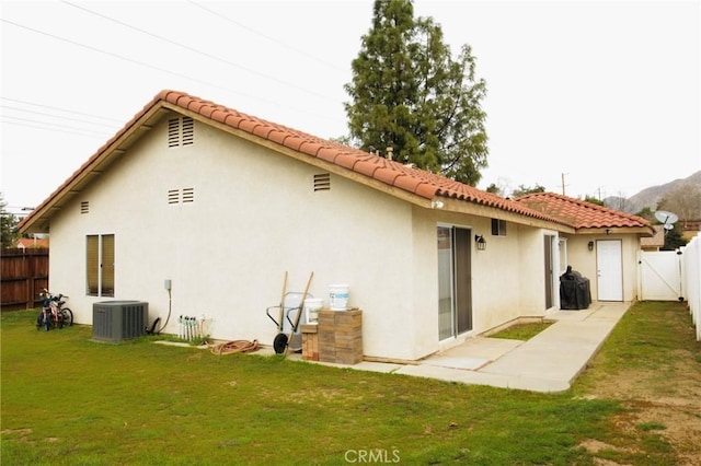 rear view of house with central AC unit, a fenced backyard, a lawn, stucco siding, and a patio area