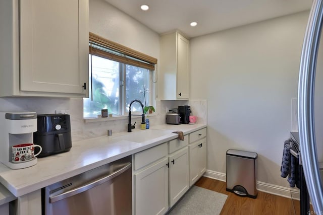 kitchen with stainless steel dishwasher, white cabinets, a sink, wood finished floors, and baseboards