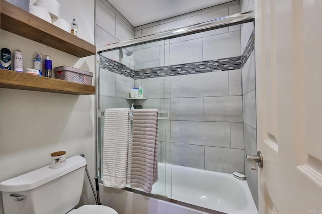 bathroom featuring toilet and shower / bath combination with glass door