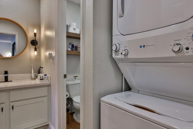 laundry area with a textured wall, stacked washer / dryer, laundry area, and a sink